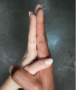 Couple's hands together with "LOVE" tattooed across their fingers, symbolizing romantic commitment and connection.